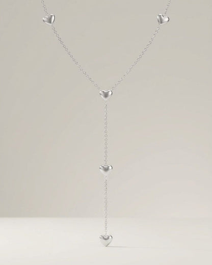 Silver y-necklace featuring a delicate chain spaced with five polished, puffy heart charms.