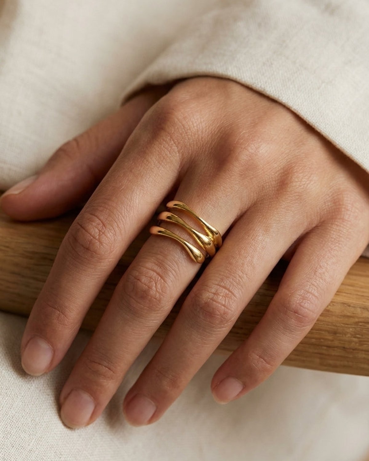 Polished gold wave stack ring worn on a hand, featuring three interconnected organic curved bands.