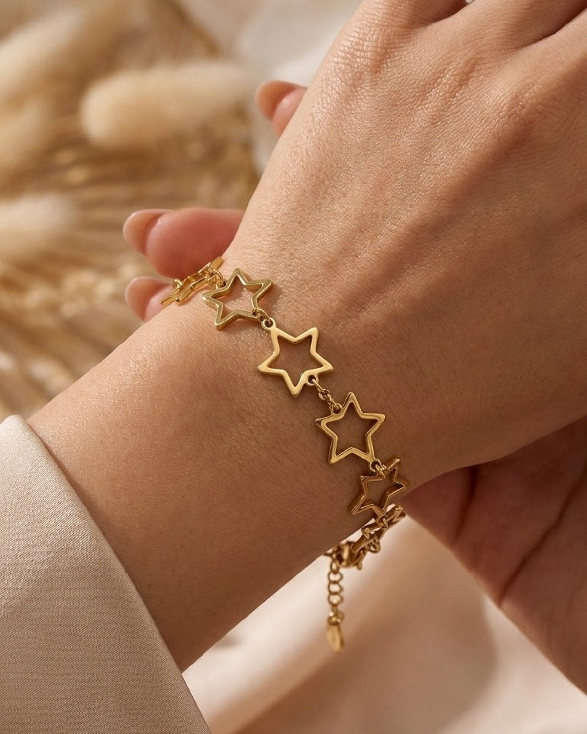 Gold metal chain bracelet with open-work star charms worn on a person's wrist.
