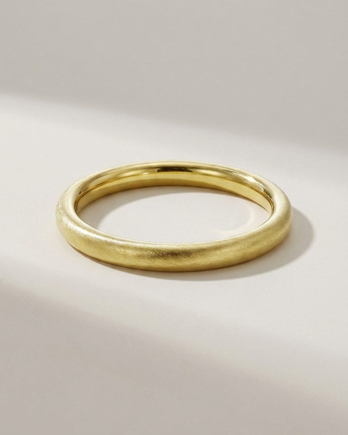 Gold bangle with a textured, brushed finish and smooth rounded profile on a light surface.