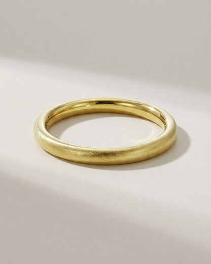 Gold bangle with a textured, brushed finish and smooth rounded profile on a light surface.