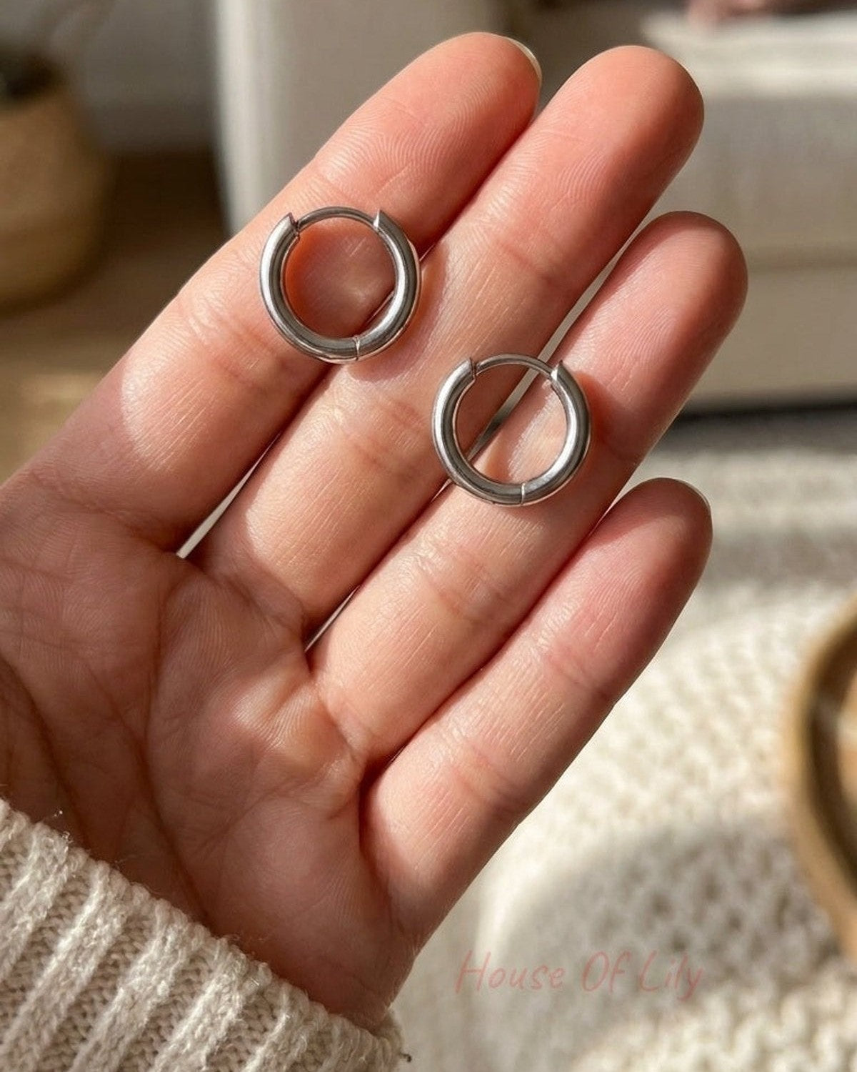 Minimalist silver hoop earrings held in a hand, featuring a simple, smooth, and circular design.