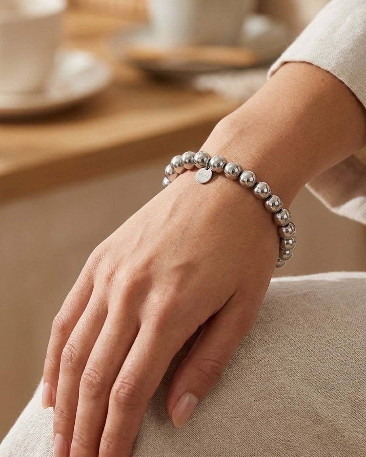 A polished silver ball bead bracelet with a small round pendant on a woman’s wrist.