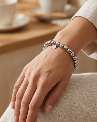 A polished silver ball bead bracelet with a small round pendant on a woman’s wrist.