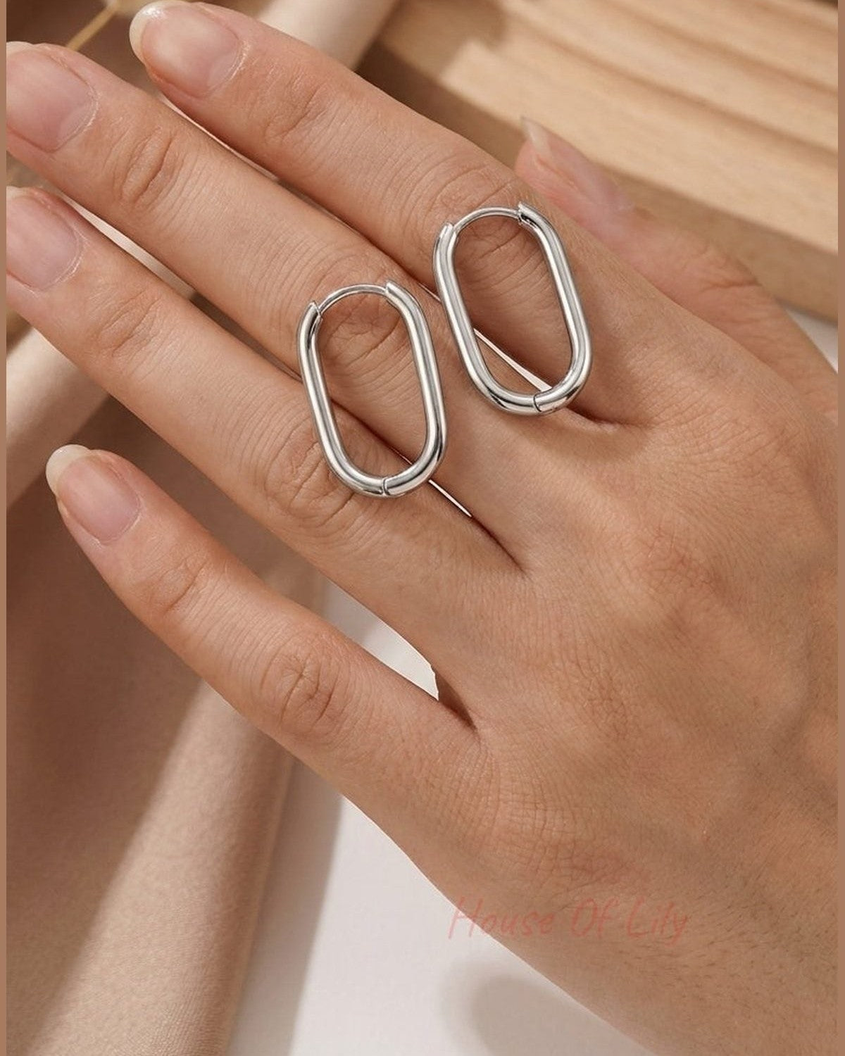 Minimalist silver oval hoop earrings held on a hand, featuring a sleek, polished modern design.
