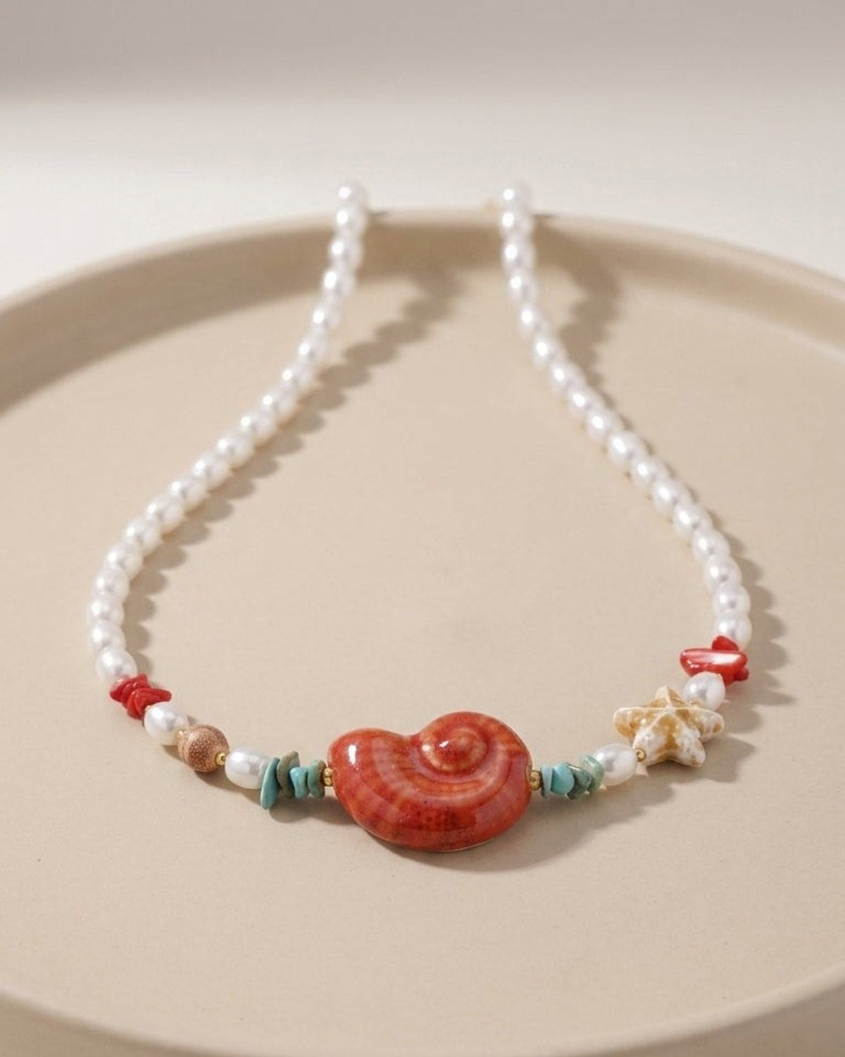 Beaded pearl necklace featuring a large red shell pendant, small turquoise chips, red accents, and a starfish charm.