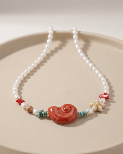 Beaded pearl necklace featuring a large red shell pendant, small turquoise chips, red accents, and a starfish charm.