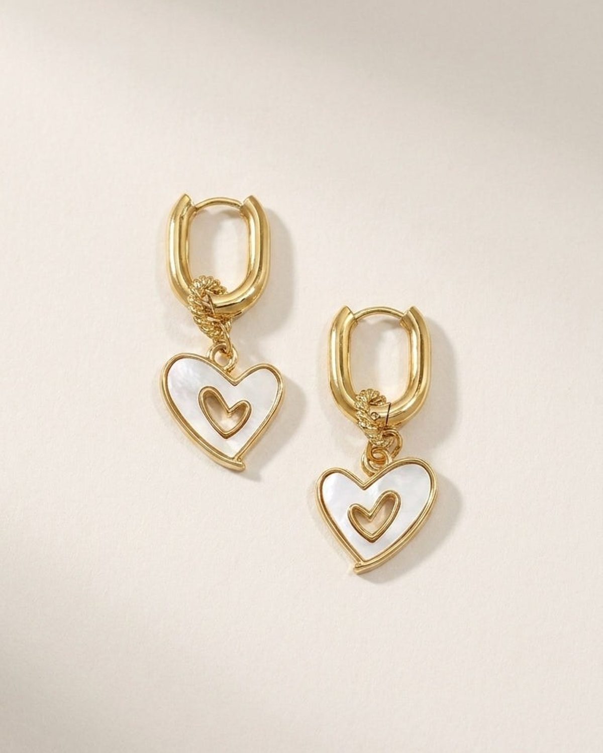 Gold hoop earrings with dangling heart charms inlaid with white mother-of-pearl and a small gold heart inside.