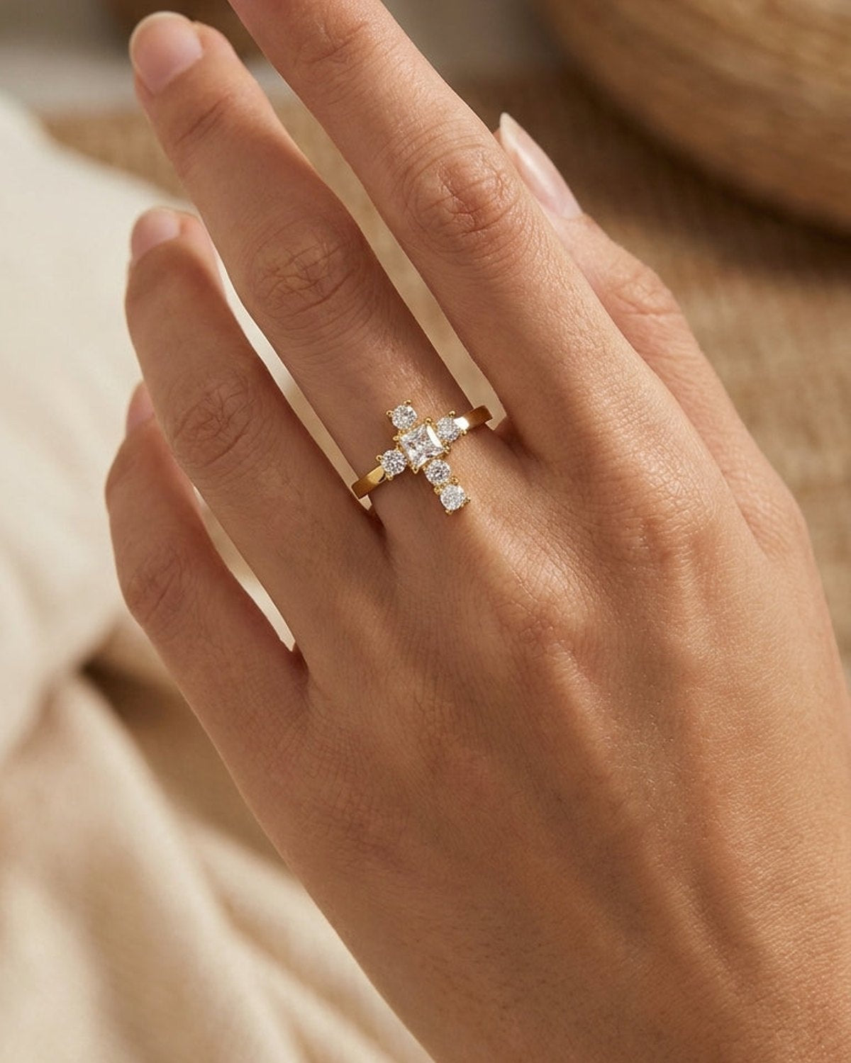Gold ring with a cross-shaped face set with five clear stones, worn on a finger.
