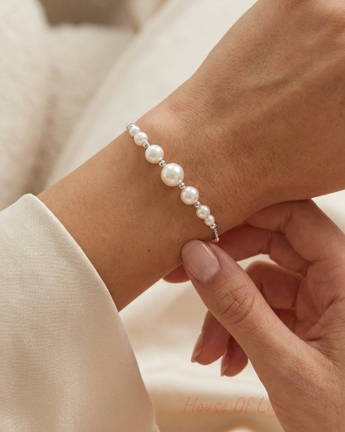 A pearl bracelet worn on a wrist, featuring graduated white round pearls separated by small silver beads.