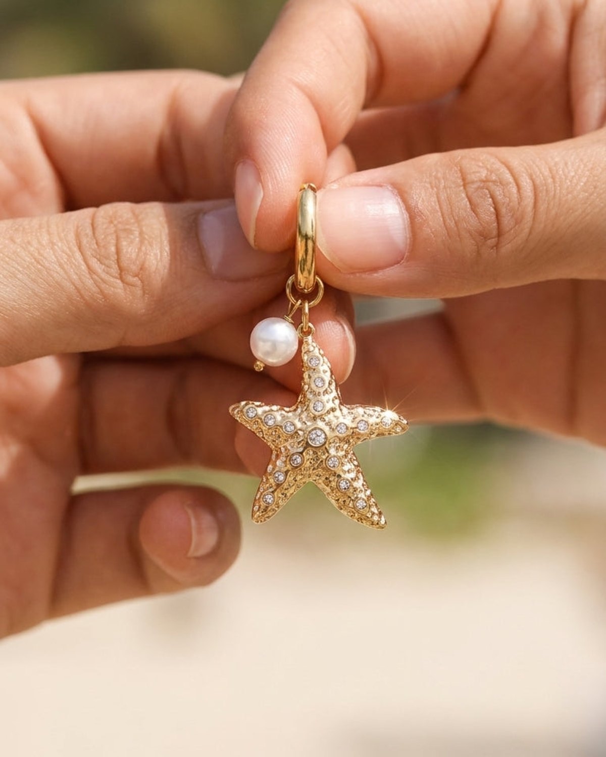 Gold hoop earring featuring a textured starfish charm with embedded crystals and a dangling white pearl.