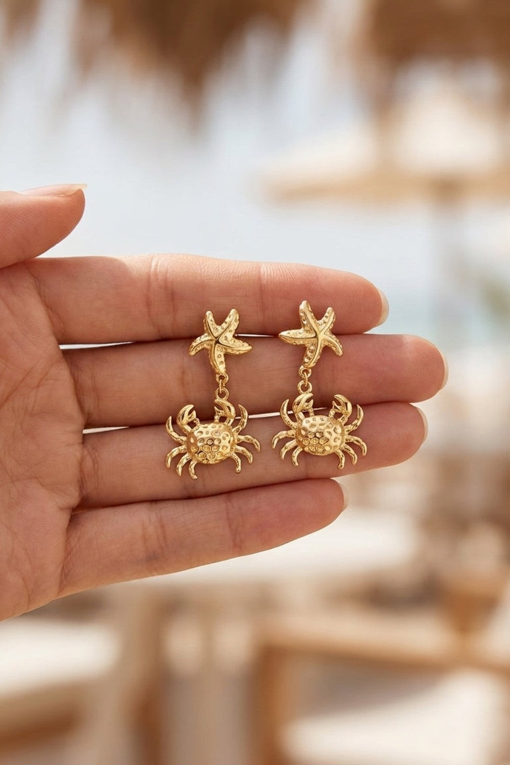 Gold drop earrings featuring a starfish stud connected by a small loop to a textured crab pendant.