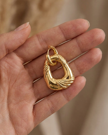 Gold irregular drop earring resting in a hand, featuring a twisted, grooved design and polished finish.