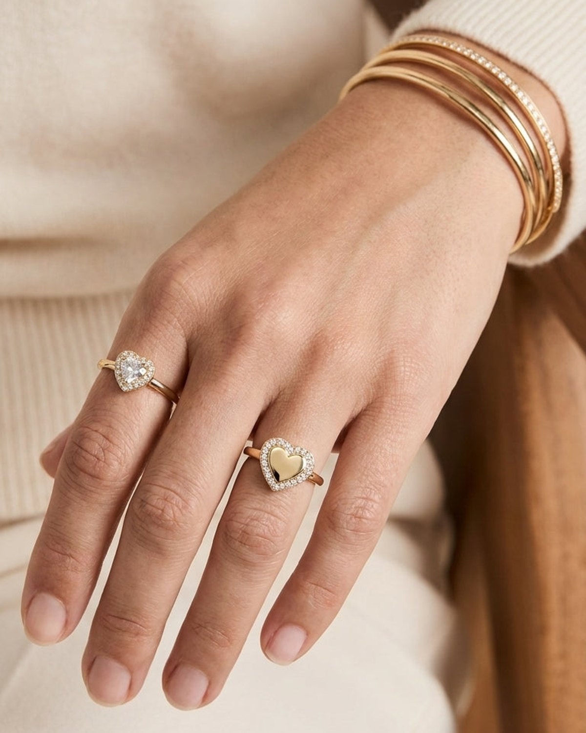 Gold heart-shaped ring with a pavé zircon halo on a hand wearing matching rings and bracelets.
