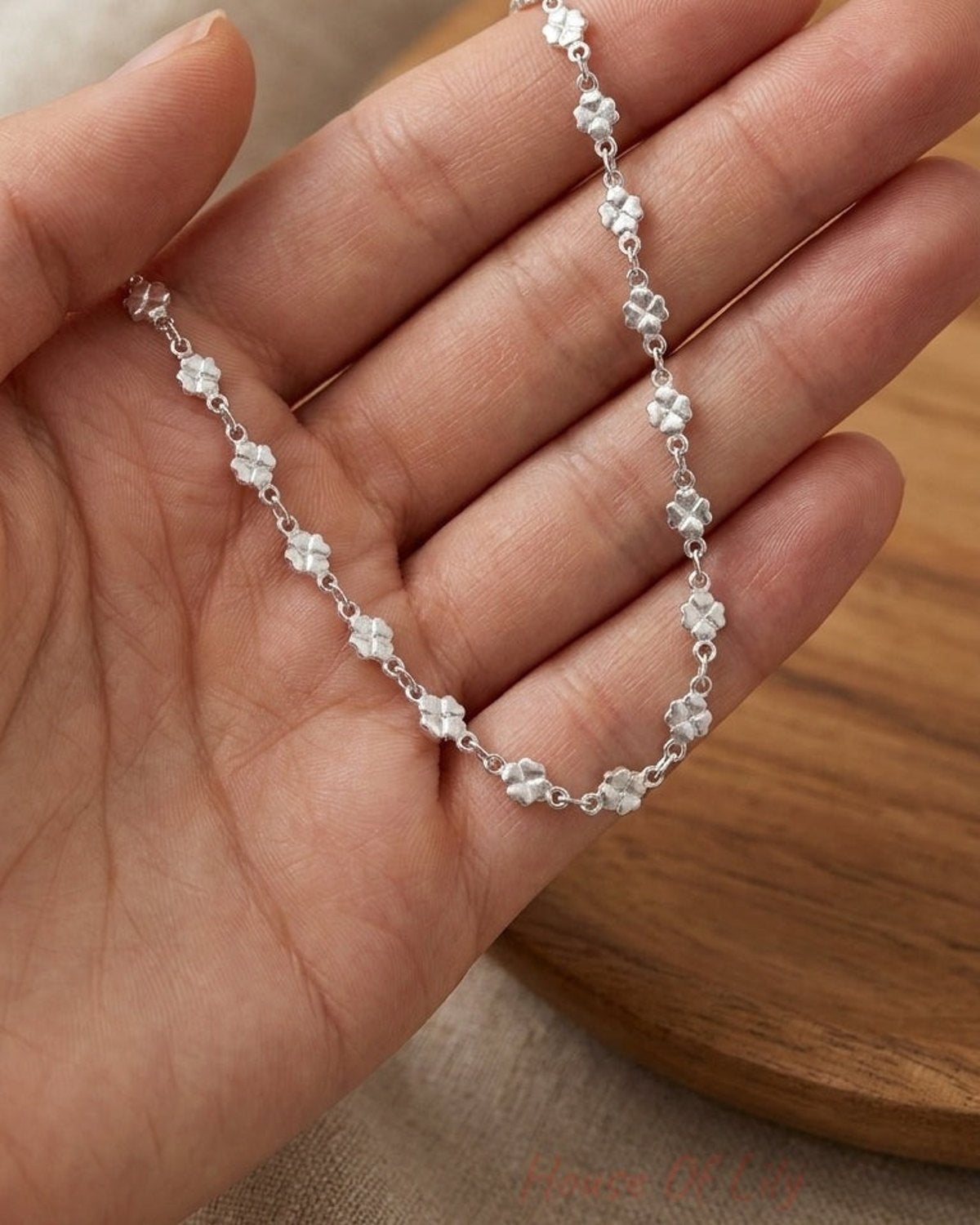 Dainty silver bracelet featuring a continuous chain of small lucky clover charms held in an open palm.