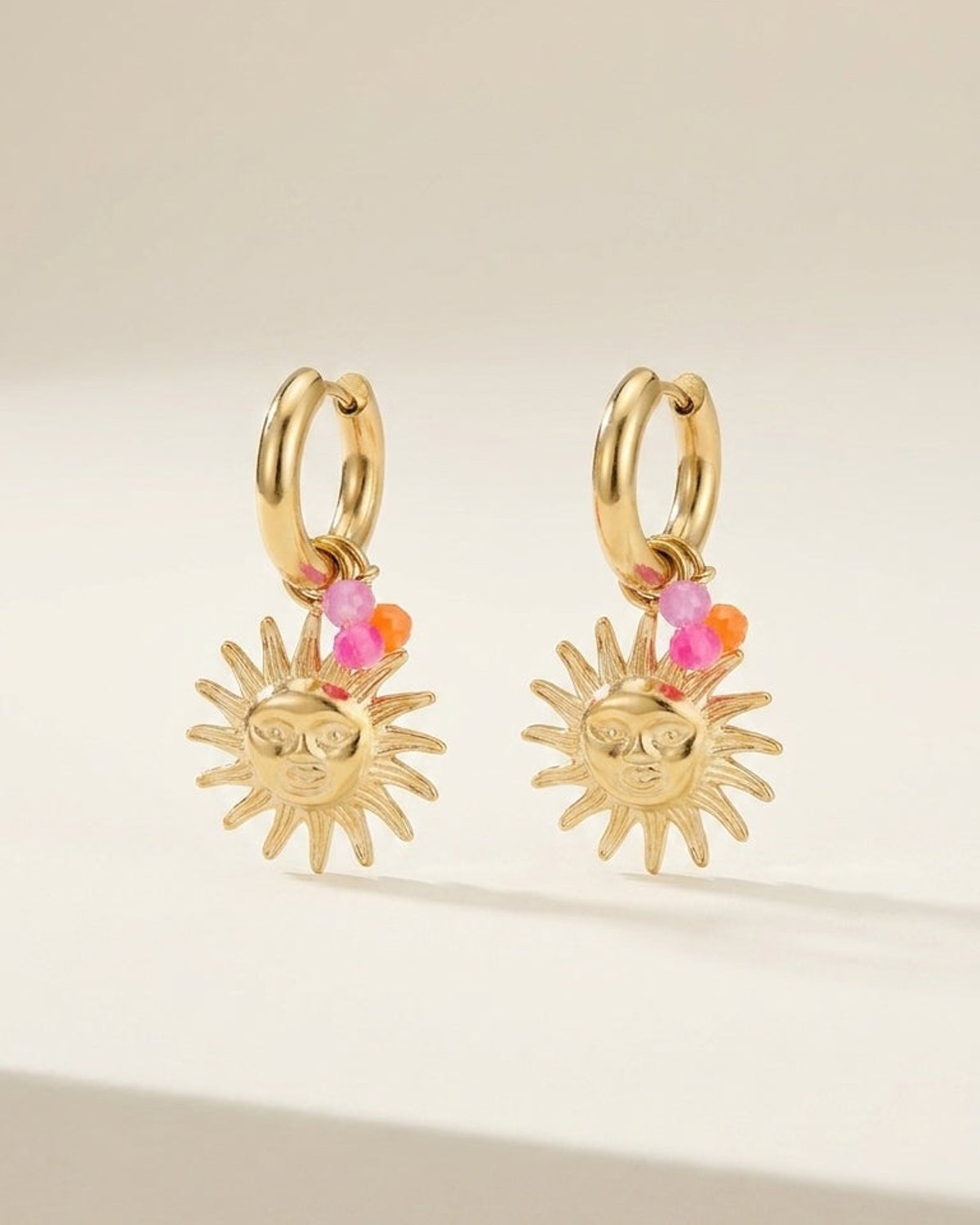 Gold hoop earrings with dangling sun charms featuring a facial design and tiny pink and orange bead accents.