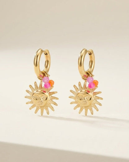 Gold hoop earrings with dangling sun charms featuring a facial design and tiny pink and orange bead accents.