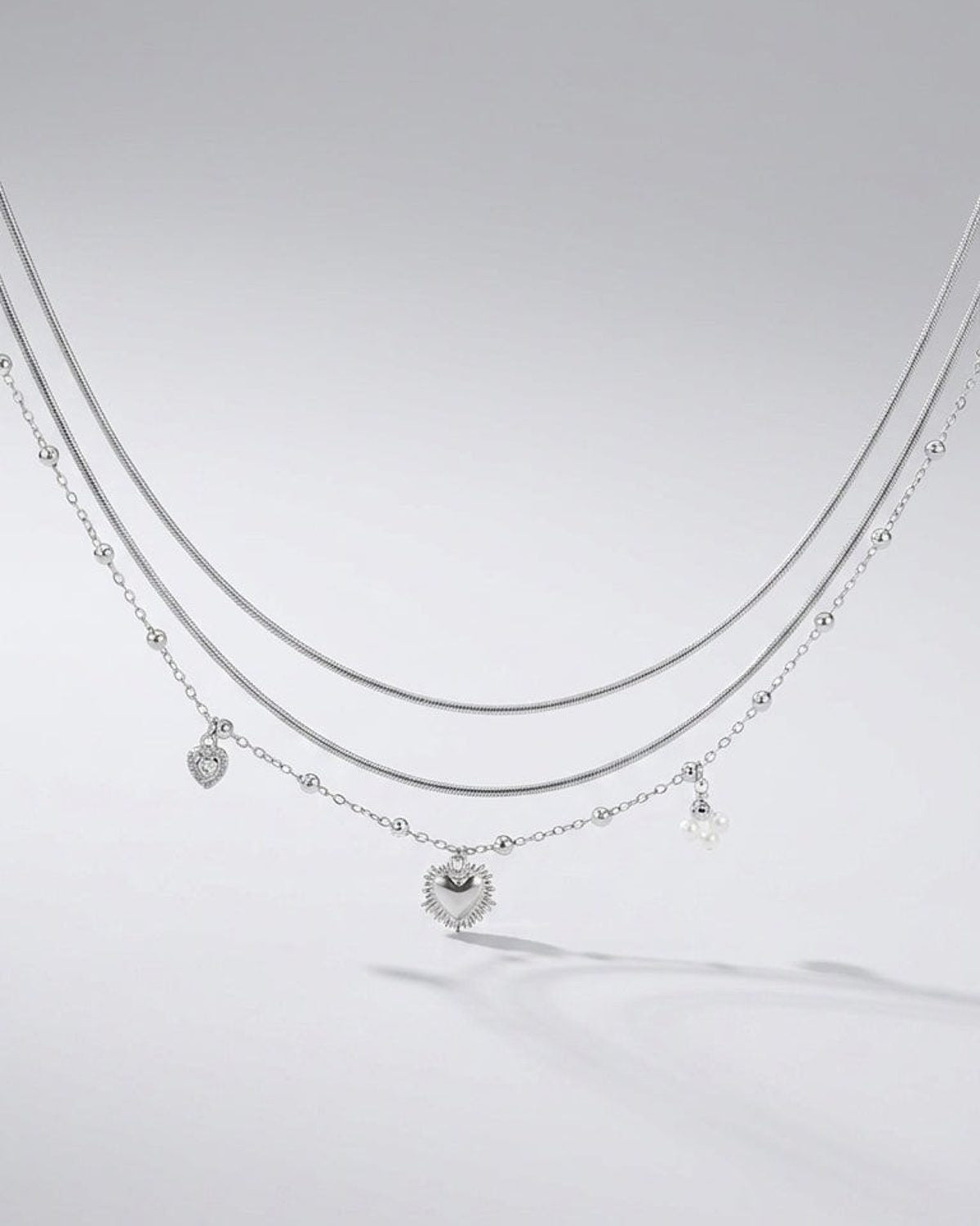 Silver layered necklace featuring a coquette heart charm, delicate bead accents, and small pearl drops.
