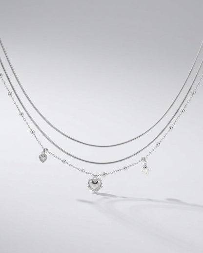 Silver layered necklace featuring a coquette heart charm, delicate bead accents, and small pearl drops.