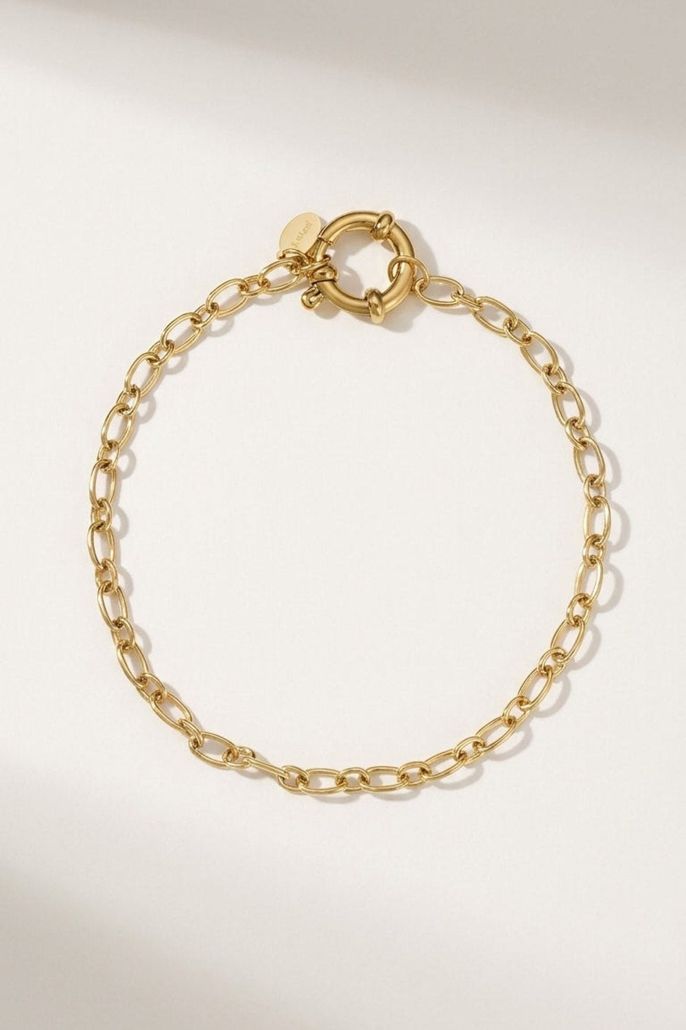 Gold oval-link chain bracelet with a front toggle clasp and small round brand tag.