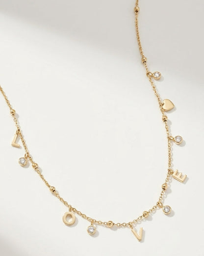 Gold letter pendant necklace spelling "LOVE" with dangling cubic zirconia stones and a small heart charm.