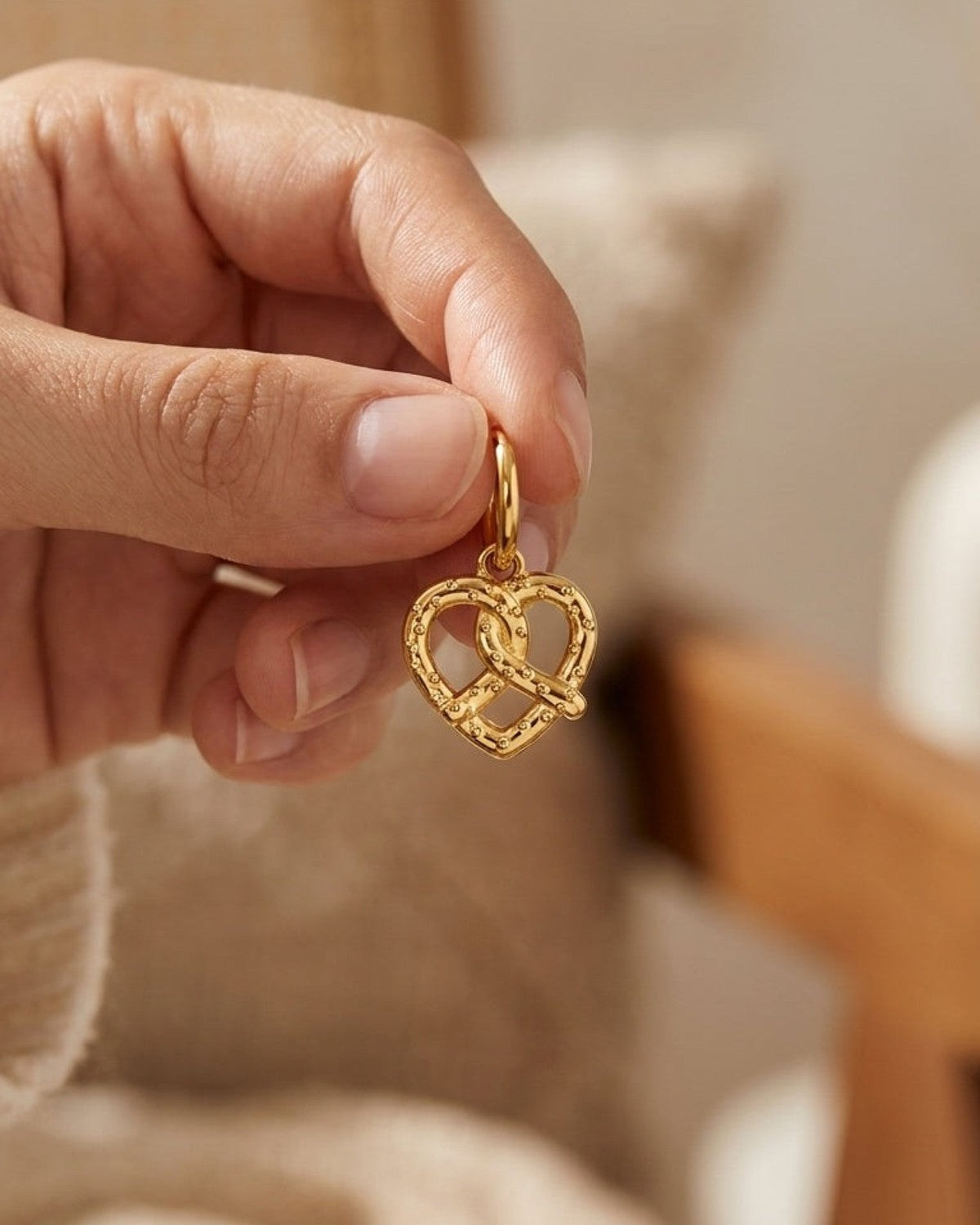 House Of Lily drop earring featuring a gold-toned metal pretzel-shaped charm held by a hand.