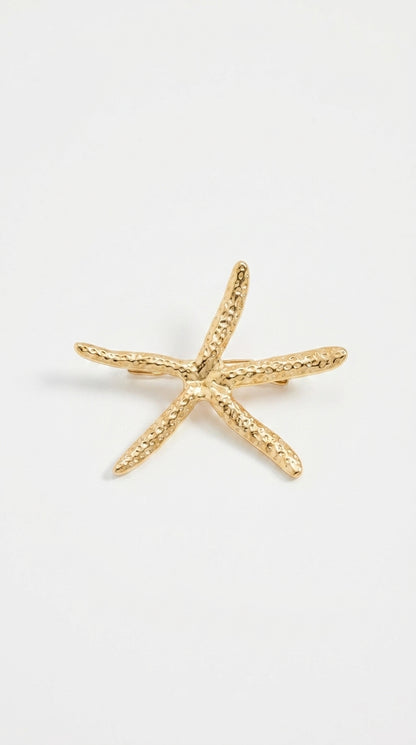 Gold-toned starfish brooch with a textured, hammered metal finish on a plain white background.