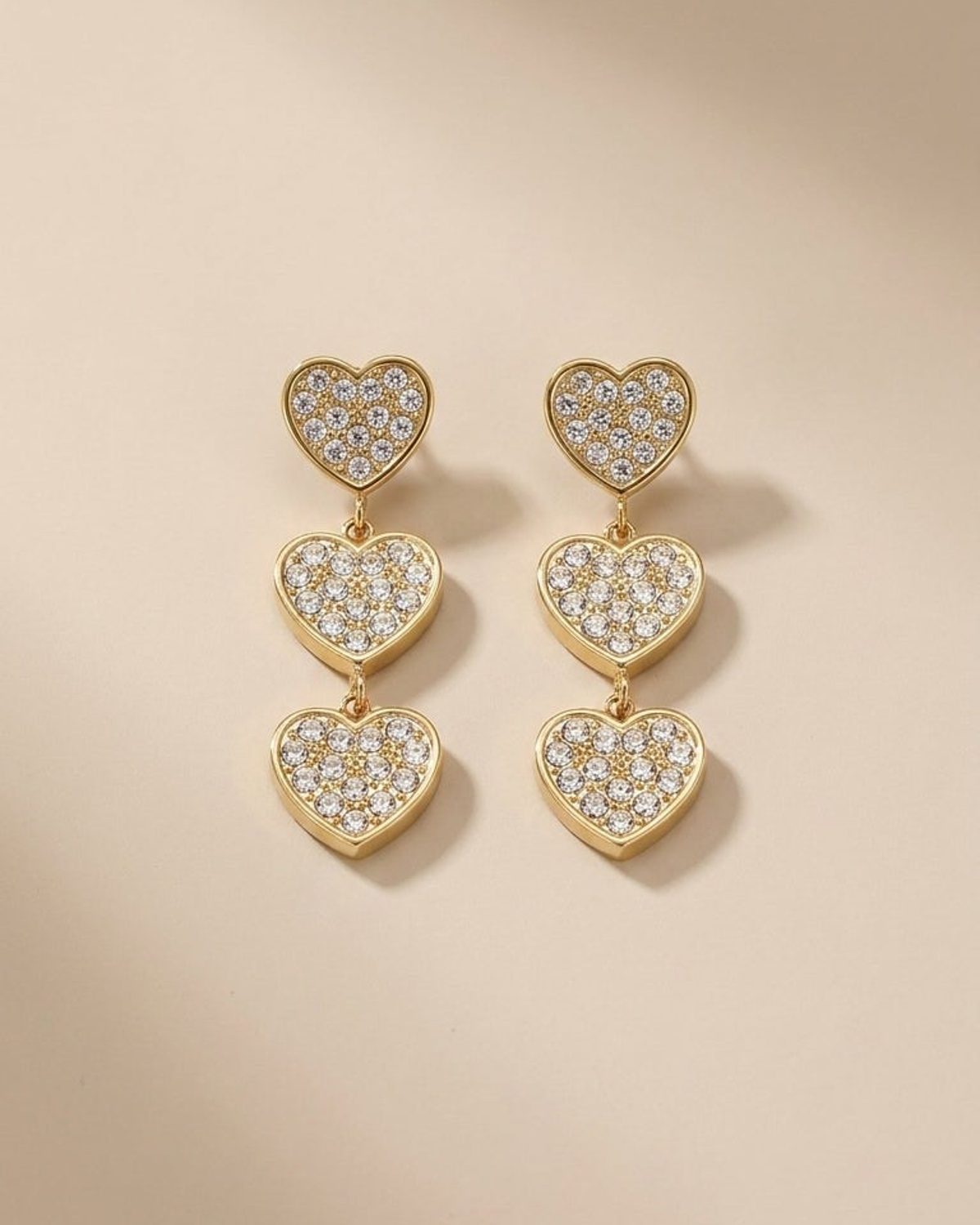 Gold-tone dangle earrings featuring three pavé-set crystal hearts arranged vertically on each.
