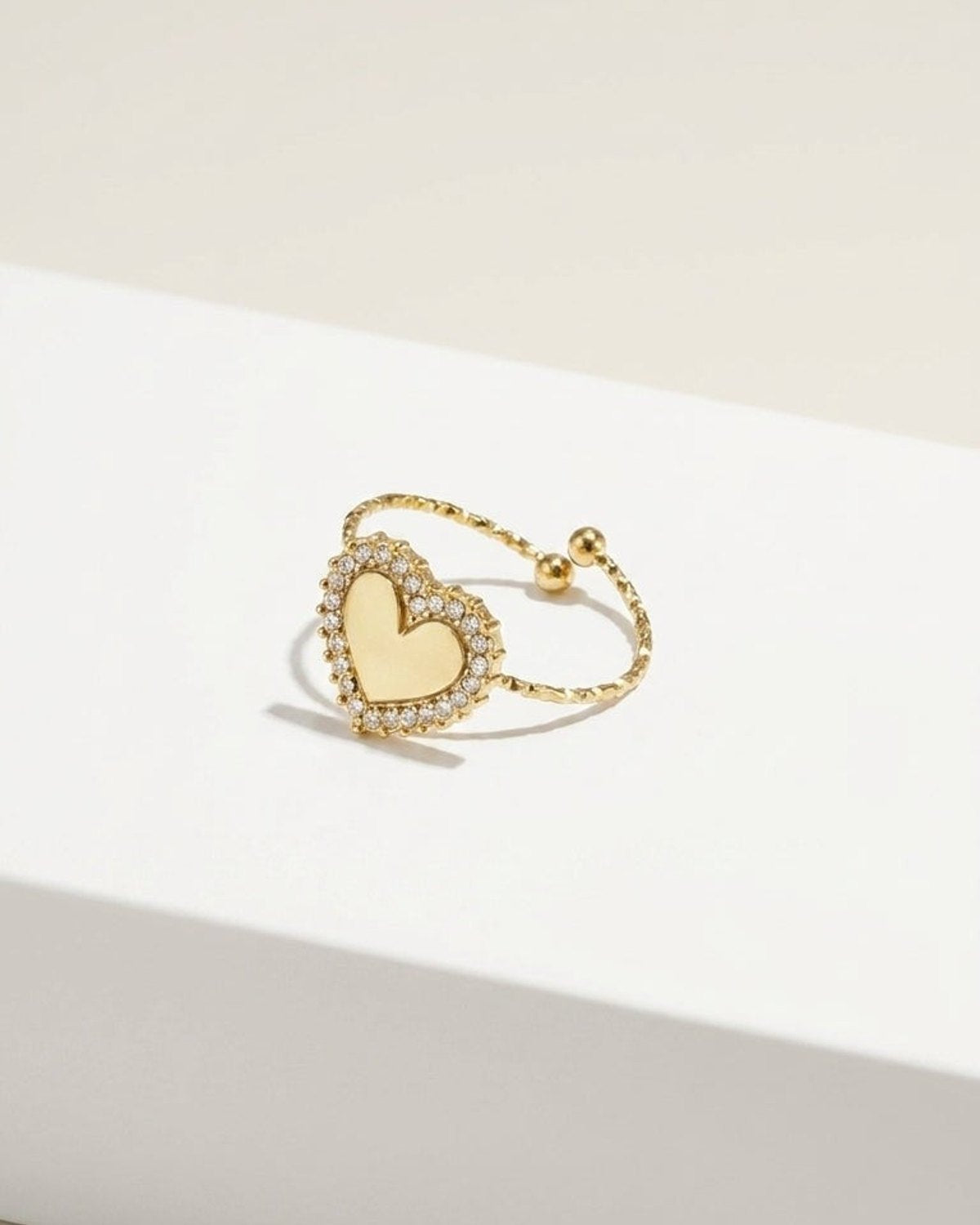 Gold adjustable ring with a pavé-set crystal heart on a white surface.