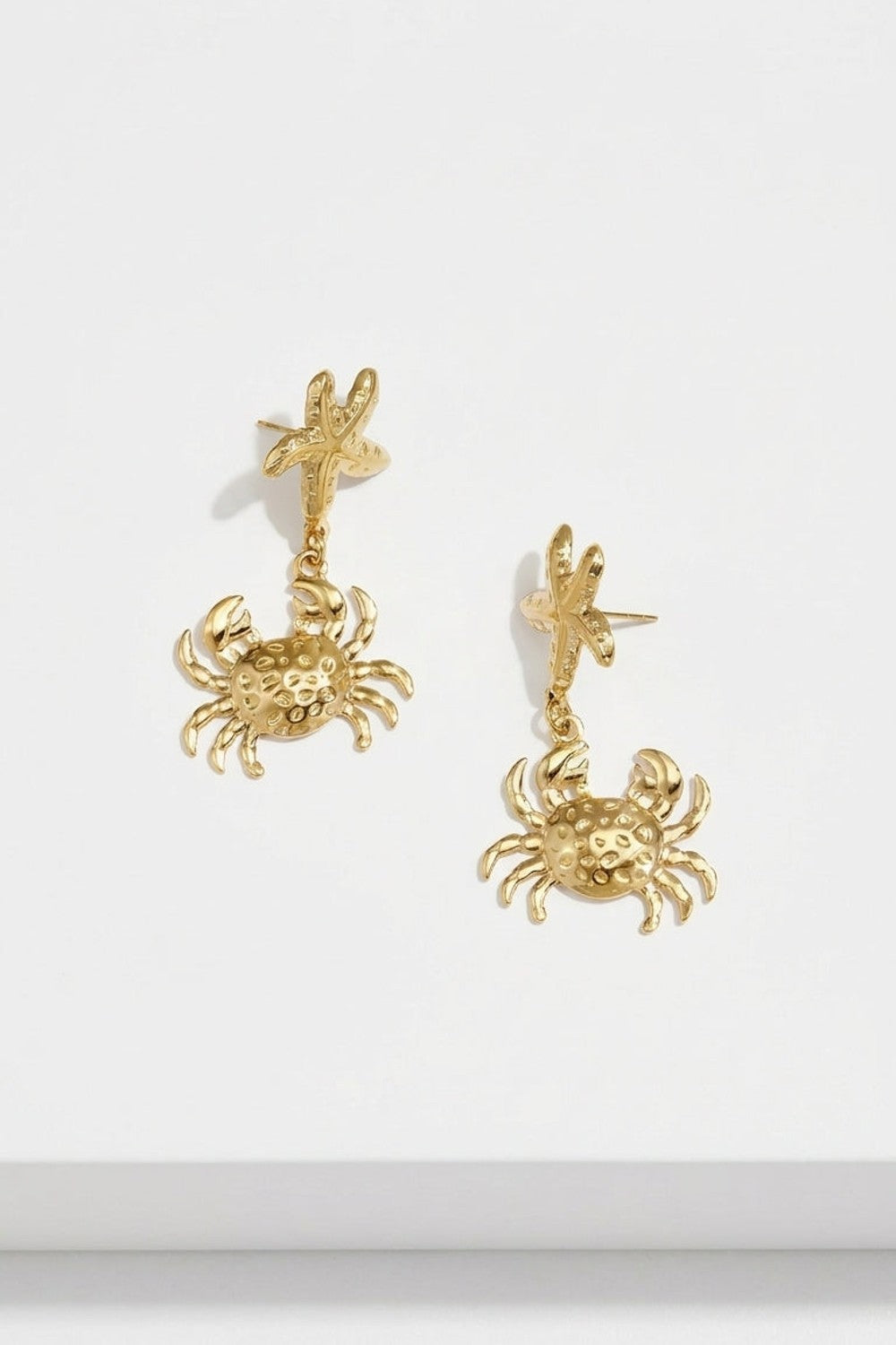 Gold drop earrings featuring a textured starfish post and a dangling crab pendant.