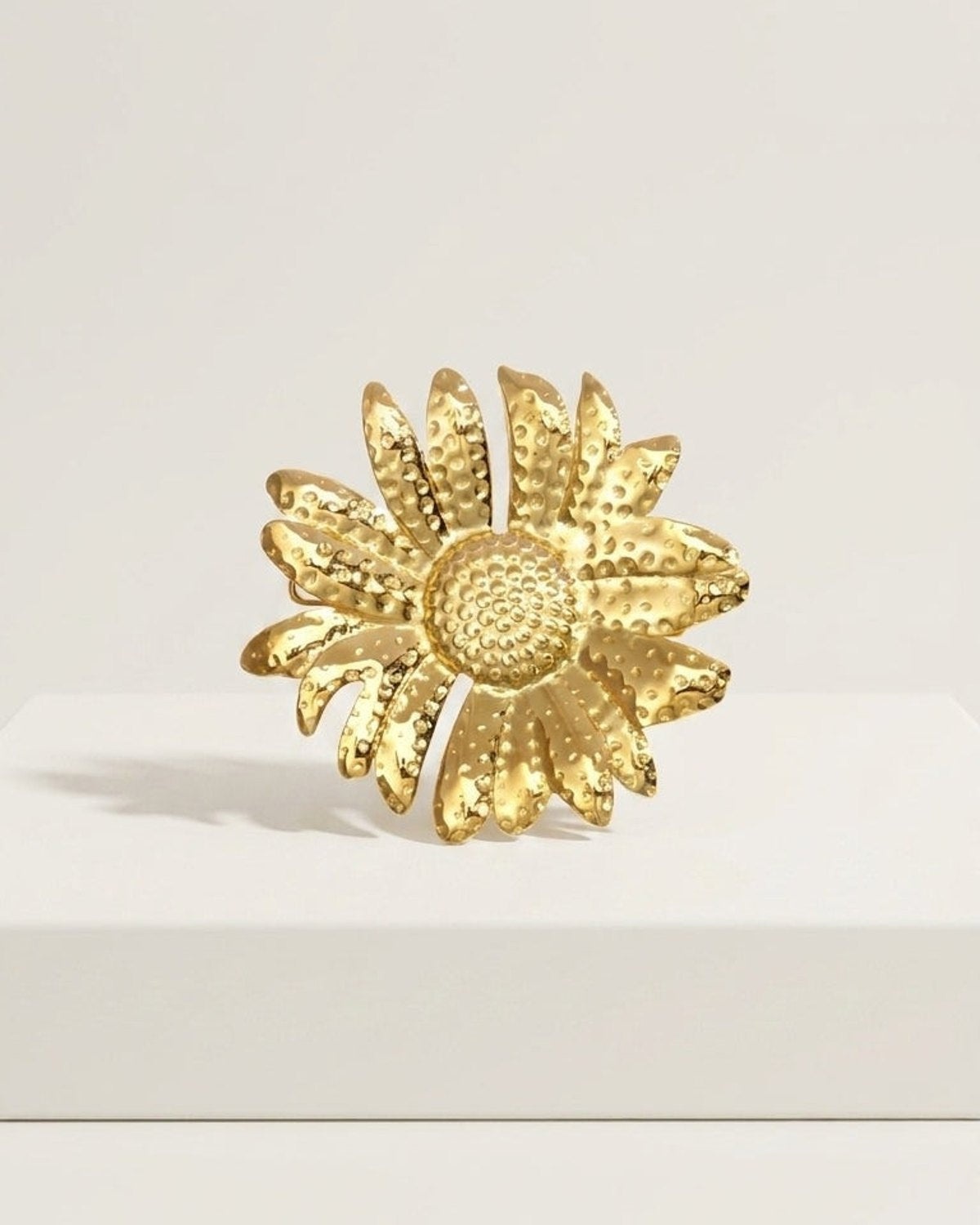 Textured gold flower brooch on a white surface.