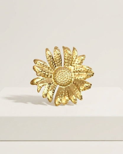 Textured gold flower brooch on a white surface.