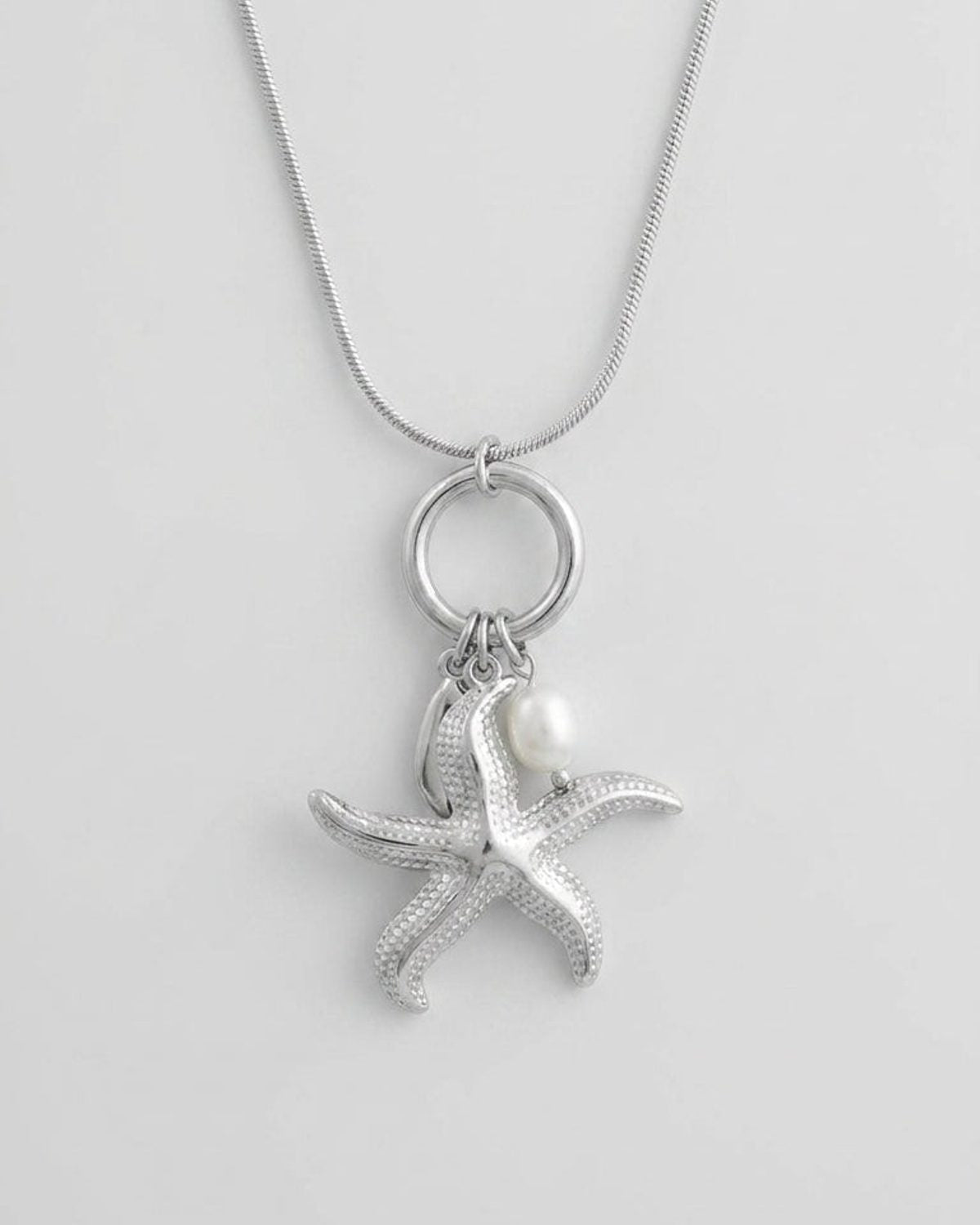 Silver-tone pendant necklace with a textured starfish charm and a white pearl bead on a round bail and snake chain.