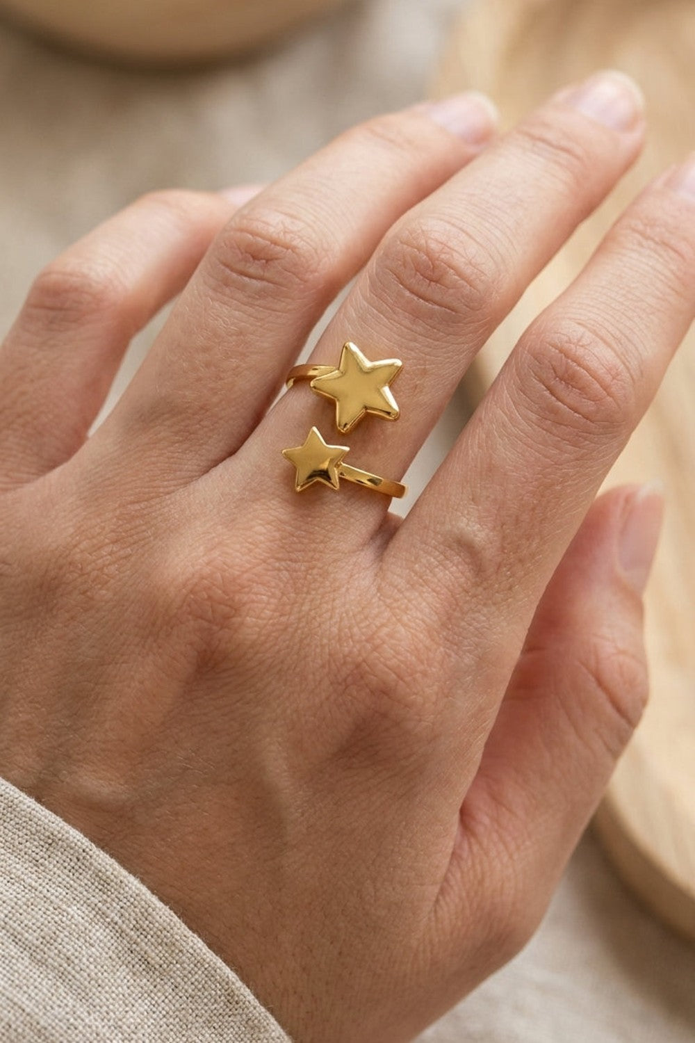 Minimalist gold-tone star ring worn on a finger, featuring two overlapping star motifs.