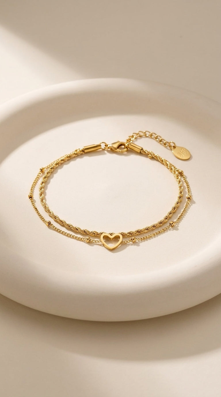 Layered gold chain bracelet with a rope texture strand and a delicate strand featuring an open heart charm.