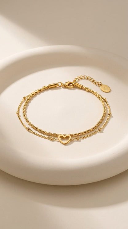 Layered gold chain bracelet with a rope texture strand and a delicate strand featuring an open heart charm.