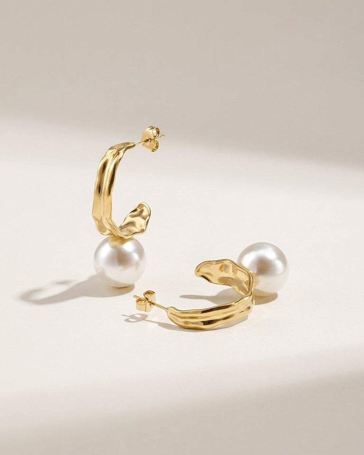 Gold drop earrings featuring irregular textured metal hoops paired with large white faux pearls.