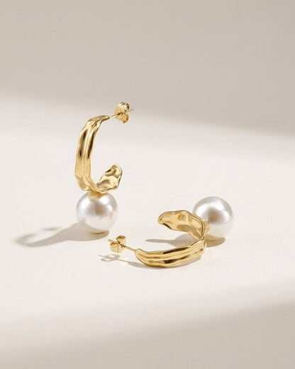 Gold drop earrings featuring irregular textured metal hoops paired with large white faux pearls.