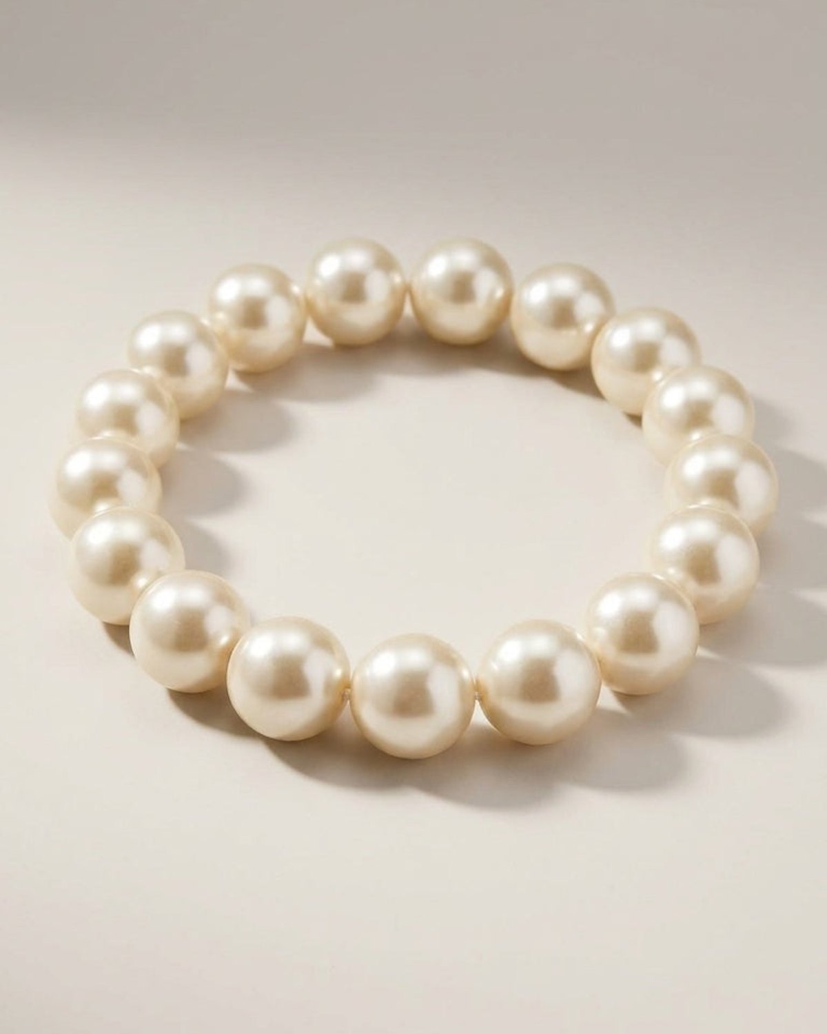 A single strand of large, lustrous cream-colored pearls arranged in a circular bracelet on a neutral surface.