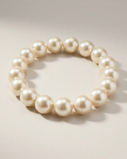A single strand of large, lustrous cream-colored pearls arranged in a circular bracelet on a neutral surface.
