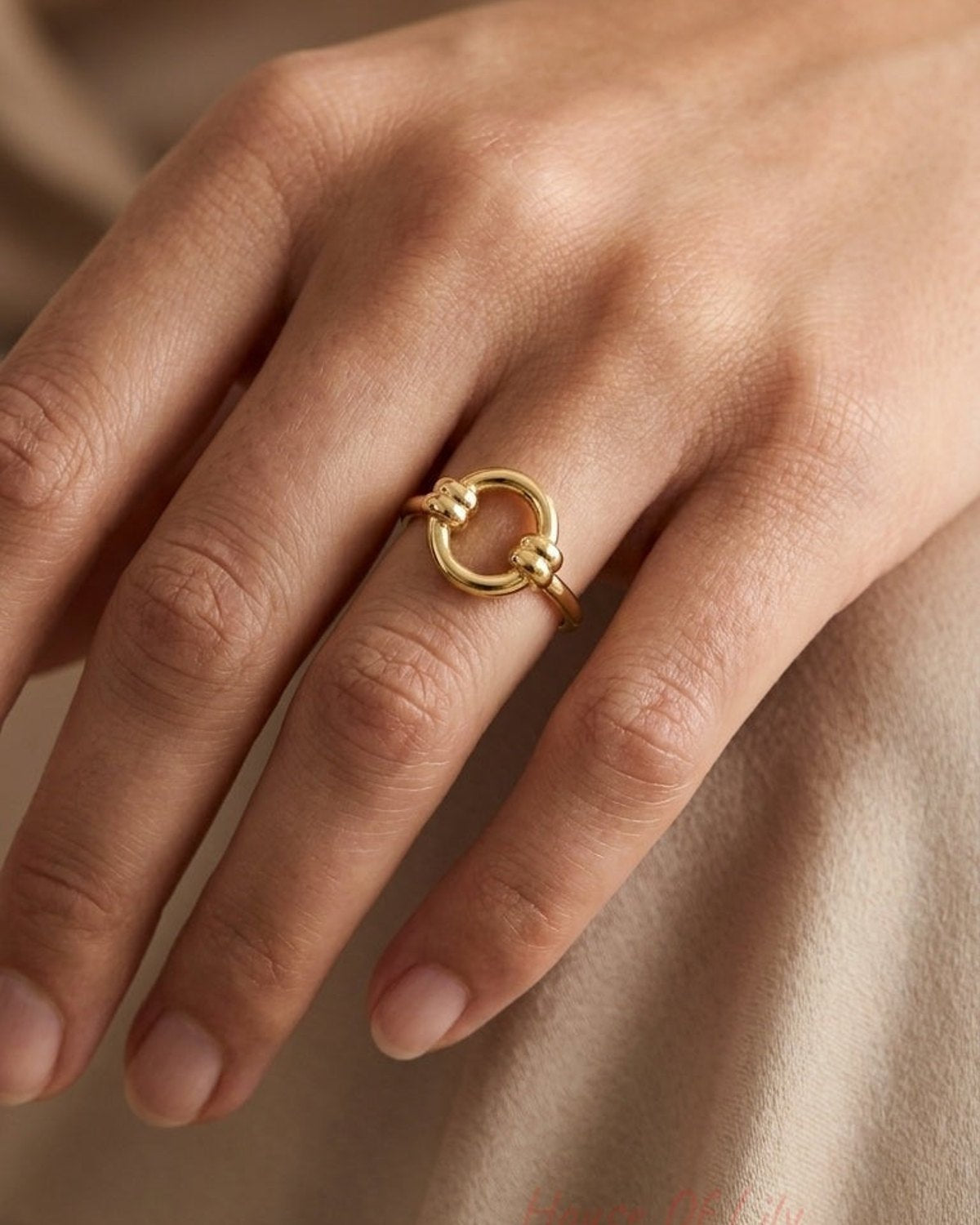 Polished gold ring featuring a circular center design with two knotted accents.