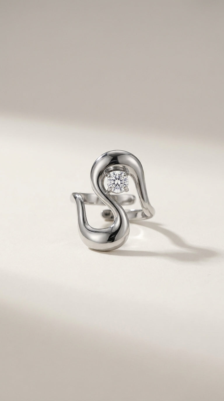 An irregular silver statement ring with an abstract wavy design holding a single round stone.