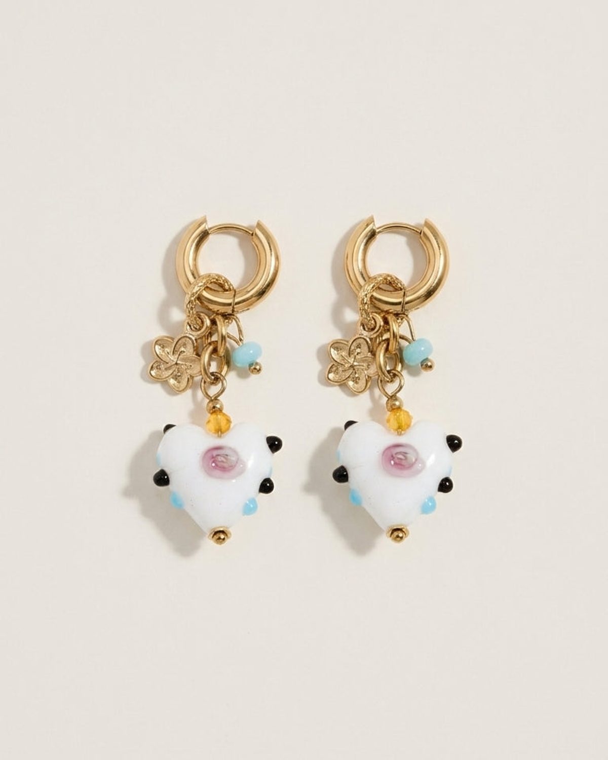 Gold hoop drop earrings with white heart charms featuring pink centers and colorful bead accents.