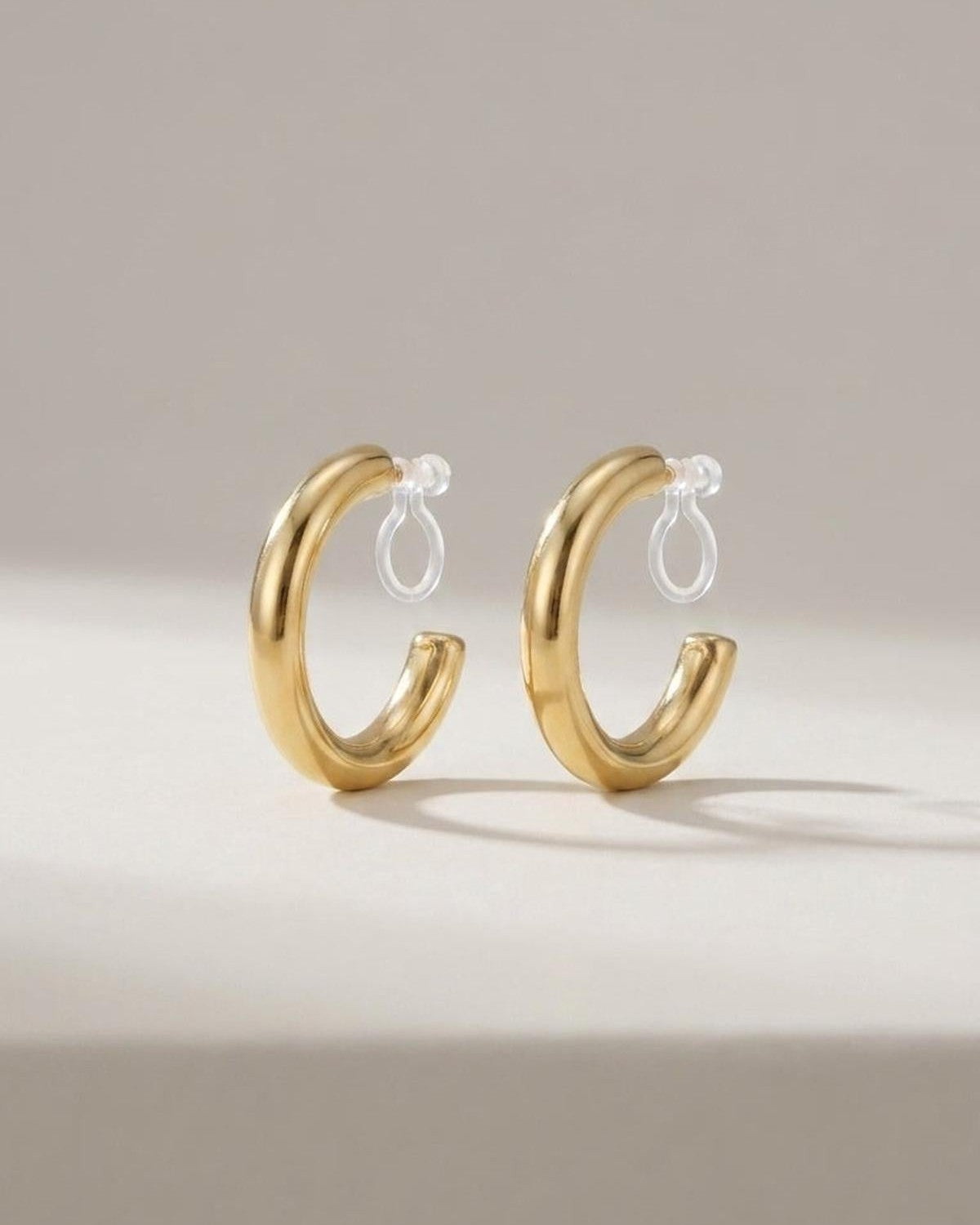 Thick gold hoop earrings with clear clip-on backs, displayed standing upright on a plain surface.