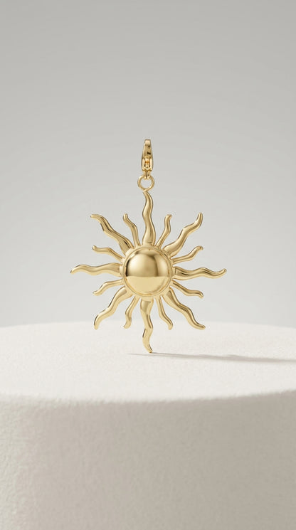 Polished gold sun jewelry charm with a smooth round center and wavy, flame-like rays.