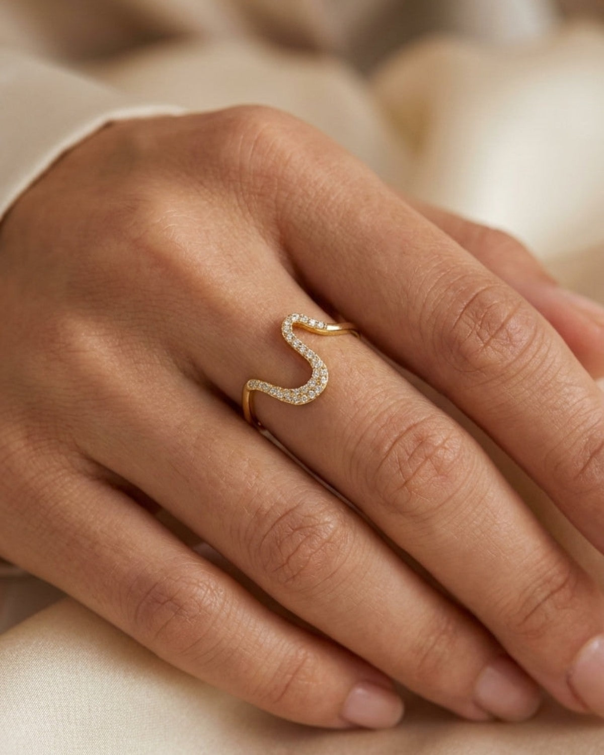 A gold Rhinestone Line Ring with a wavy, serpentine design embedded with small sparkling rhinestones on a hand.