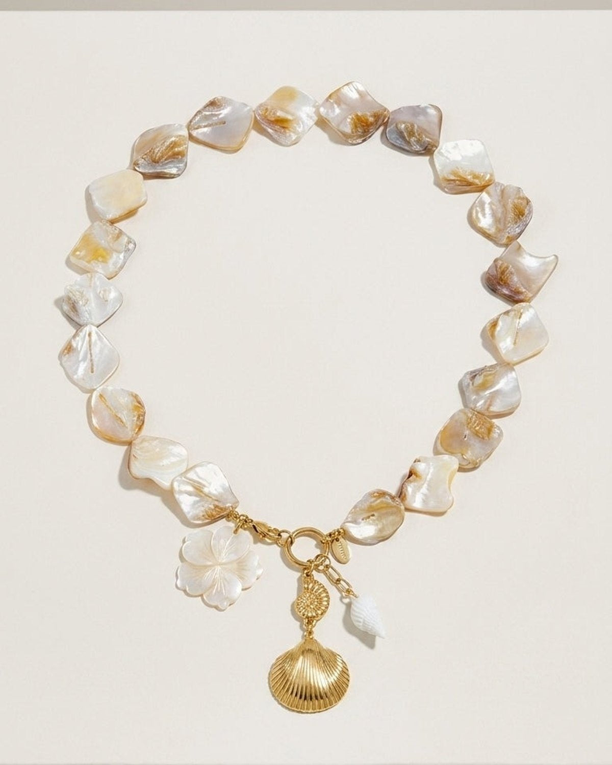 Chunky nacre bead necklace with a gold clasp, flower charm, and hanging seashell pendants.