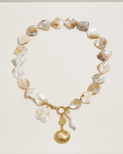 Chunky nacre bead necklace with a gold clasp, flower charm, and hanging seashell pendants.
