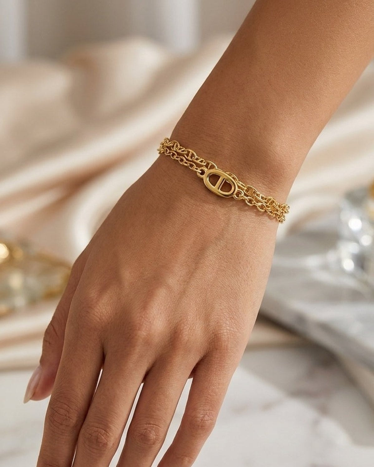 A multi-layered gold bracelet with a central link charm worn on a person's wrist.