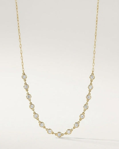 Gold chain necklace featuring evenly spaced round bezel-set stones along the lower drop against a plain background.